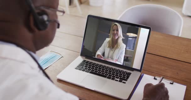 Médico Afroamericano Con Auriculares Tomando Notas Mientras Hace Una Videollamada — Vídeo de stock