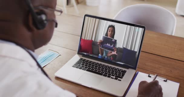 Médico Afroamericano Con Auriculares Tomando Notas Mientras Hace Una Videollamada — Vídeo de stock