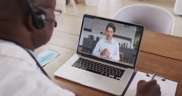 Amerykański Lekarz Słuchawkach Robi Notatki Podczas Rozmowy Wideo Laptopie Koncepcja — Wideo stockowe