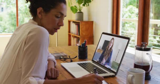 アフリカ系アメリカ人の女性は 自宅のノートパソコンでビデオ通話をしている間にメモを取る 家庭の概念から — ストック動画