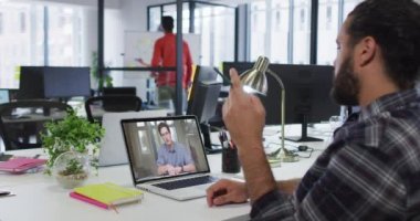 Karışık ırk işadamı, erkek meslektaşıyla görüntülü konuşma yapmak için dizüstü bilgisayar kullanıyor. Modern bir ofiste çalışıyorum..