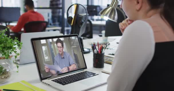 男性同僚とビデオ通話をするラップトップを使用してデスクに座っている白人の実業家 近代的なオフィスで働いていて — ストック動画