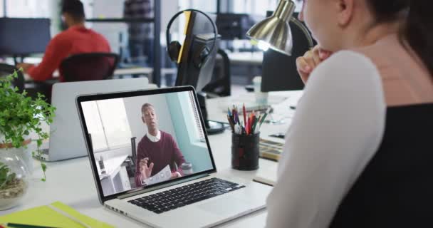 男性同僚とビデオ通話をするラップトップを使用してデスクに座っている白人の実業家 近代的なオフィスで働いていて — ストック動画