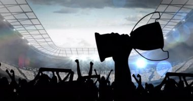 Spor fanatiklerinin siluetleri spor stadyumunun üzerinde kupa tutarken tezahürat yapıyor. Spor etkinliği ve yarışma konsepti dijital olarak oluşturulmuş video.