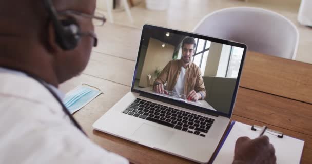 Médico Afroamericano Con Auriculares Tomando Notas Mientras Hace Una Videollamada — Vídeo de stock