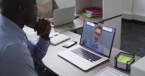 アフリカ系アメリカ人のシニア男性がオフィスのノートパソコンで男性同僚とビデオ通話をしています ビジネス プロ意識 テクノロジーの概念 — ストック動画