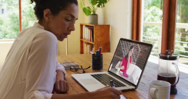 アフリカ系アメリカ人女性は 自宅のラップトップで女性同僚とビデオ通話をしている間にメモを取る 家庭の概念から — ストック動画