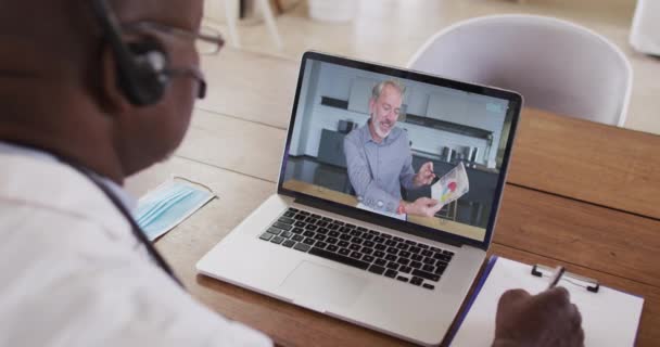 Amerykański Lekarz Słuchawkach Robi Notatki Podczas Rozmowy Wideo Laptopie Koncepcja — Wideo stockowe