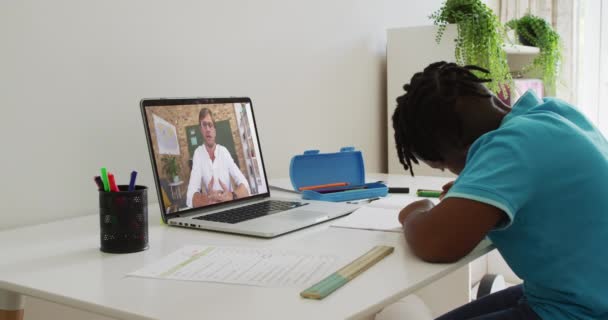 アフリカ系アメリカ人の少年は オンラインの学校の授業があるノートパソコンを使って机に座っている 隔離中に隔離された家で — ストック動画