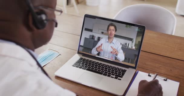 Amerykański Lekarz Słuchawkach Robi Notatki Podczas Rozmowy Wideo Laptopie Koncepcja — Wideo stockowe