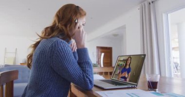 Beyaz kadın, telefon kulaklığı takıyor. Ev bilgisayarında iş arkadaşıyla görüntülü görüşme yapıyor. ev kavramından çalışma