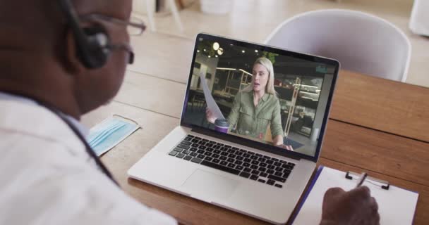 Amerykański Lekarz Słuchawkach Robi Notatki Podczas Rozmowy Wideo Laptopie Koncepcja — Wideo stockowe