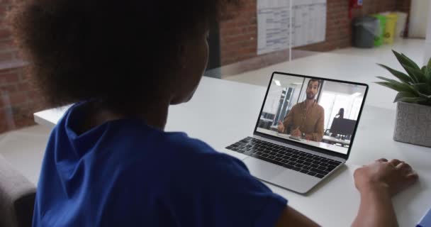 アフリカ系アメリカ人女性のバックビューオフィスでラップトップで男性同僚とビデオ通話をしています ビジネス リモートワーク テクノロジーの概念は — ストック動画