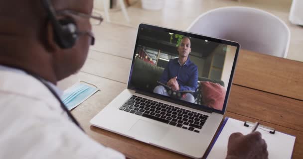 Amerykański Lekarz Słuchawkach Robi Notatki Podczas Rozmowy Wideo Laptopie Koncepcja — Wideo stockowe