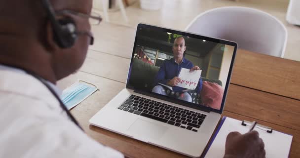 Amerykański Lekarz Słuchawkach Robi Notatki Podczas Rozmowy Wideo Laptopie Koncepcja — Wideo stockowe