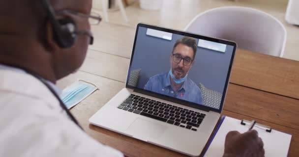 Médico Afroamericano Con Auriculares Tomando Notas Mientras Hace Una Videollamada — Vídeo de stock