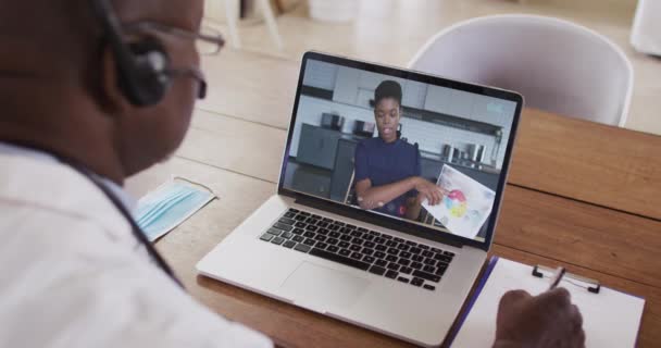 Médico Afroamericano Con Auriculares Tomando Notas Mientras Hace Una Videollamada — Vídeo de stock