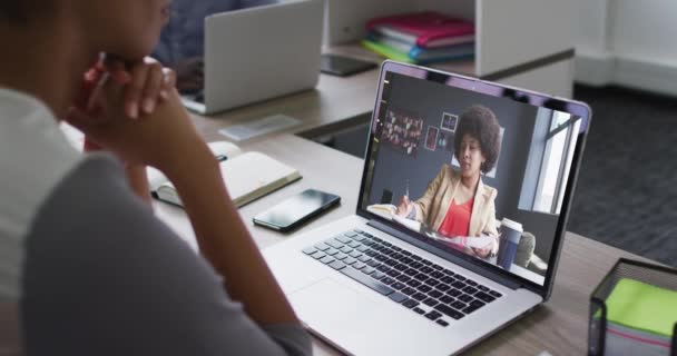 アフリカ系アメリカ人のビジネスマンは 女性の同僚とビデオ通話をするラップトップを使用してデスクに座っています 近代的なオフィスで働いていて — ストック動画