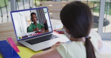 Yüz maskesi takan bir kızın evde dizüstü bilgisayarında Afro-Amerikan bir çocukla görüntülü konuşması. uzak öğrenim ve çevrimiçi eğitim kavramı