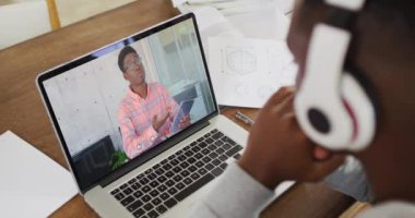 Afro-Amerikan erkek üniversite öğrencisi elinde notlar tutarken evdeki bilgisayarında bir video görüşmesi var. uzak öğrenim ve çevrimiçi eğitim kavramı