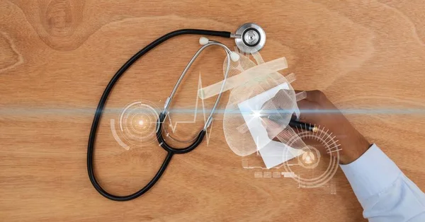 Composition of hand of doctor writing and stethoscope on desk with medical research interface screen. global medicine, research and digital interface concept digitally generated