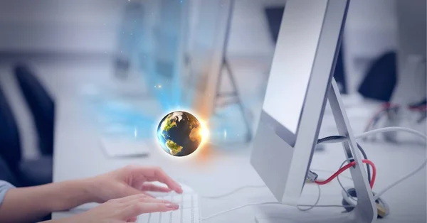 Composition of small glowing globe floating over midsection of woman using computer in office. global communication and business technology concept digitally generated image.