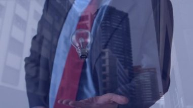 Ampulün animasyonu iş adamının elinin ve modern binaların arka planında. küresel fikirler, ağ oluşturma ve iş konsepti dijital olarak oluşturulmuş video.