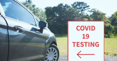 Composition of covid 19 testing text with arrow on sign over car in car park. global coronavirus pandemic concept digitally generated image.
