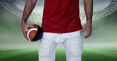 Afrika kökenli Amerikalı erkek rugby oyuncusunun ragbi topunu arka planda stadyuma karşı tutması. spor ve spor konsepti