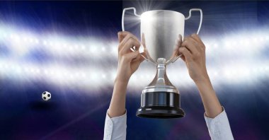 Arka plandaki spor stadyumunun spot ışıkları karşısında kupayı elinde tutan kişinin kompozisyonu. şampiyonluklar, spor ve yarışma konsepti dijital olarak oluşturulmuş imaj.