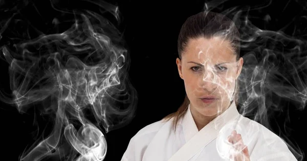 Composition of female martial artist over trails of smoke on black background. sport and competition concept digitally generated image.