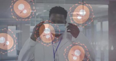 Yüz maskesi takan Afro-Amerikan erkek doktorun portresine karşı hareket eden çoklu covid-19 hücreleri. Coronavirus covid-19 salgın konsepti