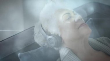 Kulaklıkla müzik dinleyen mutlu yaşlı kadının üzerinde parlayan ışığın animasyonu. emeklilik ve mutlu yaşlı yaşam konsepti dijital olarak oluşturulmuş video.