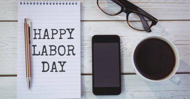 Kahve fincanı, bardaklar ve ahşap arka planda akıllı telefonlara karşı günlükte mutlu iş günü mesajları. Amerikan İşçi Bayramı şablon tasarım konsepti