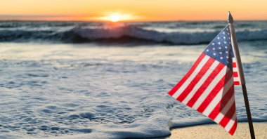 Gün batımına ve deniz kenarına Amerikan bayrağı sallama kompozisyonu. Birleşik Devletler vatanseverliği ve bağımsızlık kavramı dijital olarak oluşturuldu.