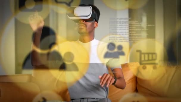 自宅でVrヘッドセットを身に着けているアフリカ系アメリカ人に対して浮かんでいる複数の黄色のデジタルアイコン エンターテイメントと未来的なテクノロジーのコンセプト — ストック動画