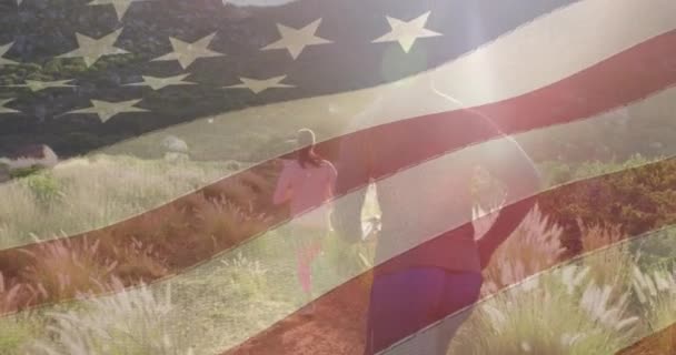 牧草地を走る夫婦の上を移動するアメリカ国旗のアニメーション 愛国心とお祝いのコンセプトをデジタルで — ストック動画