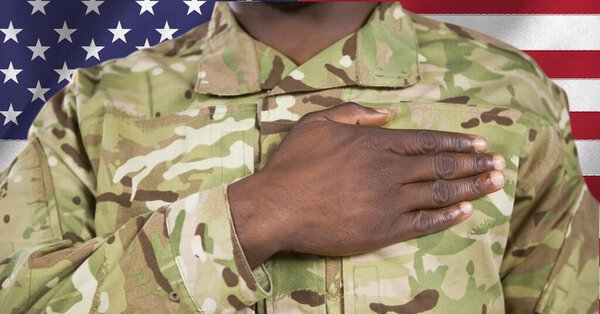 Composition of midsection of male soldier with hand on heart, against american flag. patriotism, independence and military concept digitally generated image.