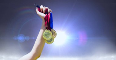 Gri arka planda ışık lekelerine karşı birden fazla madalyayı tutan eli yakın durun. Spor turnuvası ve yarışma konsepti