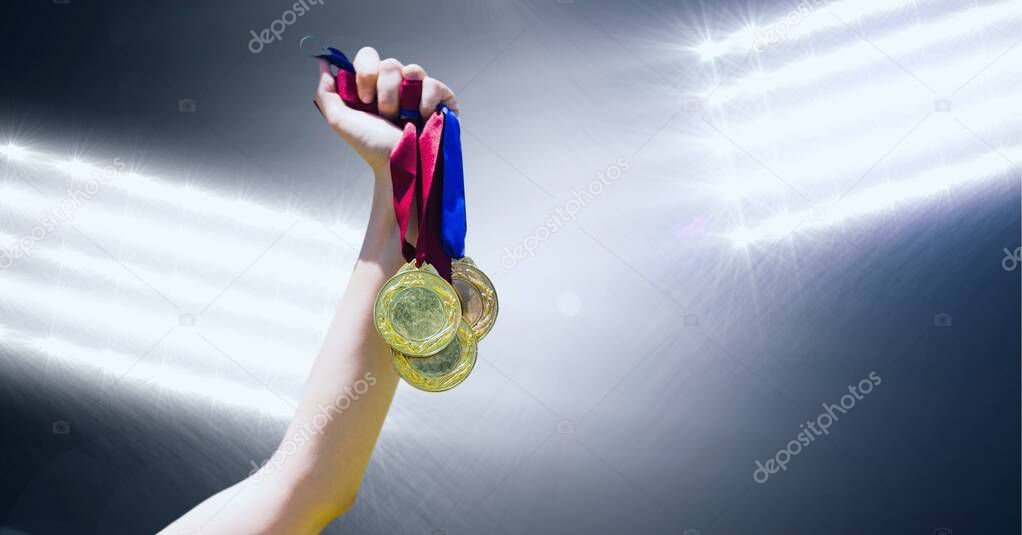 Close up of hand holding multiple medals against flood lights on black background. sports tournament and competition concept