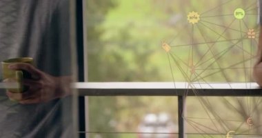 Evdeki akıllı telefonu kullanarak elinde kahve fincanı olan bir adama karşı dönen dijital ikon küresi. küresel ağ ve teknoloji kavramı