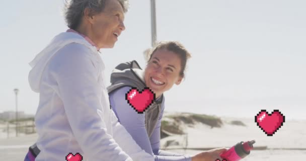 ビーチで話して幸せな女性の上に浮かんでいる赤いピクセルの心のアニメーション ポジティブな感情と幸福の概念をデジタルで生成し — ストック動画