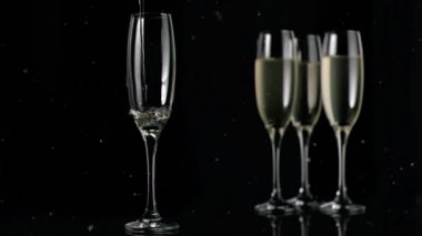 Siyah arka planda şampanya kadehlerinin üzerinde süzülen beyaz beneklerin canlandırılması. kutlama ve yeni yıl partisi konsepti dijital olarak oluşturulmuş video.
