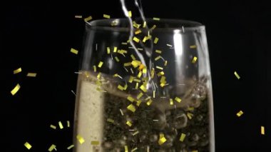 Siyah arka planda bir bardak şampanyanın üzerine düşen altın konfetilerinin animasyonu. kutlama ve yeni yıl partisi konsepti dijital olarak oluşturulmuş video.