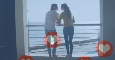 Balkonda deniz kenarında mutlu bir çiftin anısına sosyal medyanın kalp ikonlarının canlandırılması. küresel sosyal medya, bağlantılar, dijital arayüz ve teknoloji konsepti dijital olarak oluşturulmuş video.