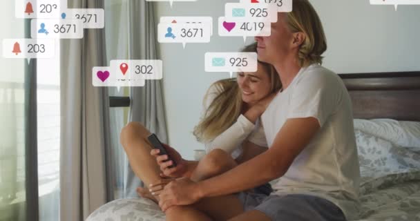 Animation Social Media Notifications Smiling Couple Sitting Bed Using Smartphone — Stock Video