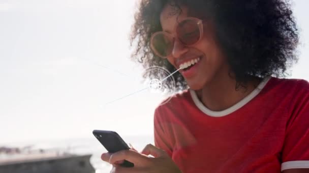 ビーチでスマートフォンを使用してアフリカ系アメリカ人女性に対するデジタルアイコンのネットワーク 世界的なネットワーキング技術の概念 — ストック動画