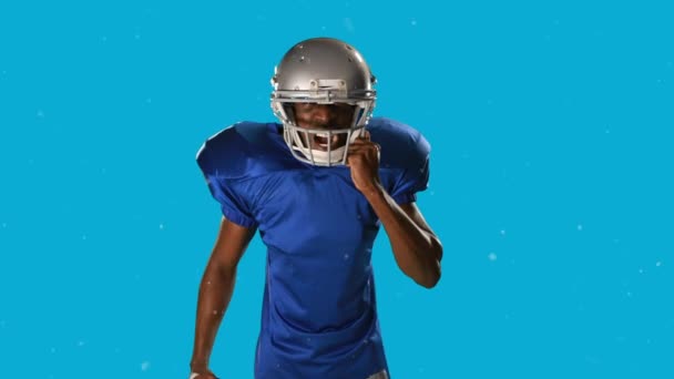 青い背景にボールを持つアメリカのサッカー選手に落ちる雪のアニメーション スポーツと競争の概念をデジタルで生成し — ストック動画