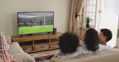 Mutlu bir ailenin evde oturup televizyonda rugby maçı izlemesinin birleşimi. spor, rekabet, eğlence ve teknoloji konsepti dijital olarak oluşturulmuş video.