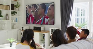 Mutlu bir ailenin evde oturup TV 'de spor müsabakalarını izlemesinin birleşimi. spor, rekabet, eğlence ve teknoloji konsepti dijital olarak oluşturulmuş video.
